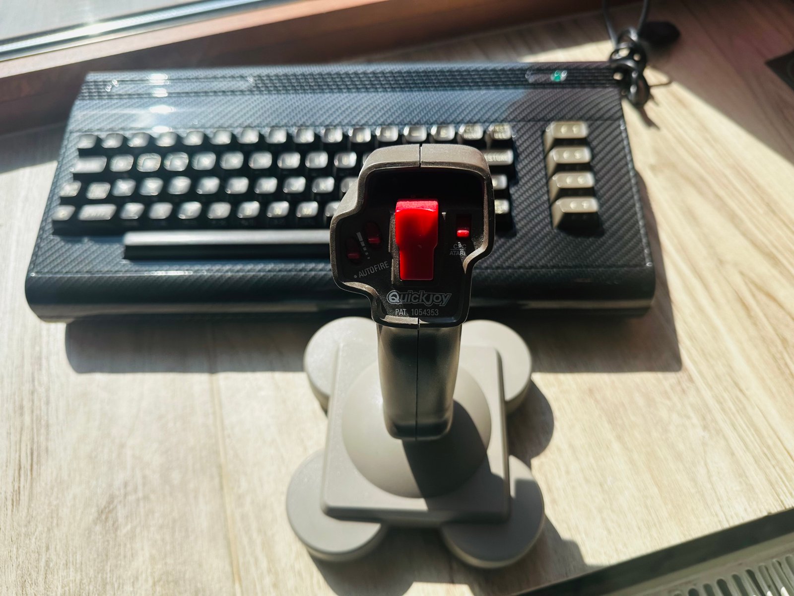 Odbudowany Commodore 64 w wykończeniu carbon fiber wraz z joystickiem QuickJoy, stojący na drewnianym biurku